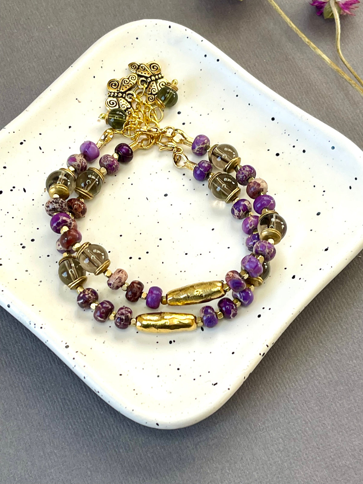 Purple imperial jasper and smoky quartz beaded bracelet with a textured gold tone bar and butterfly charm

