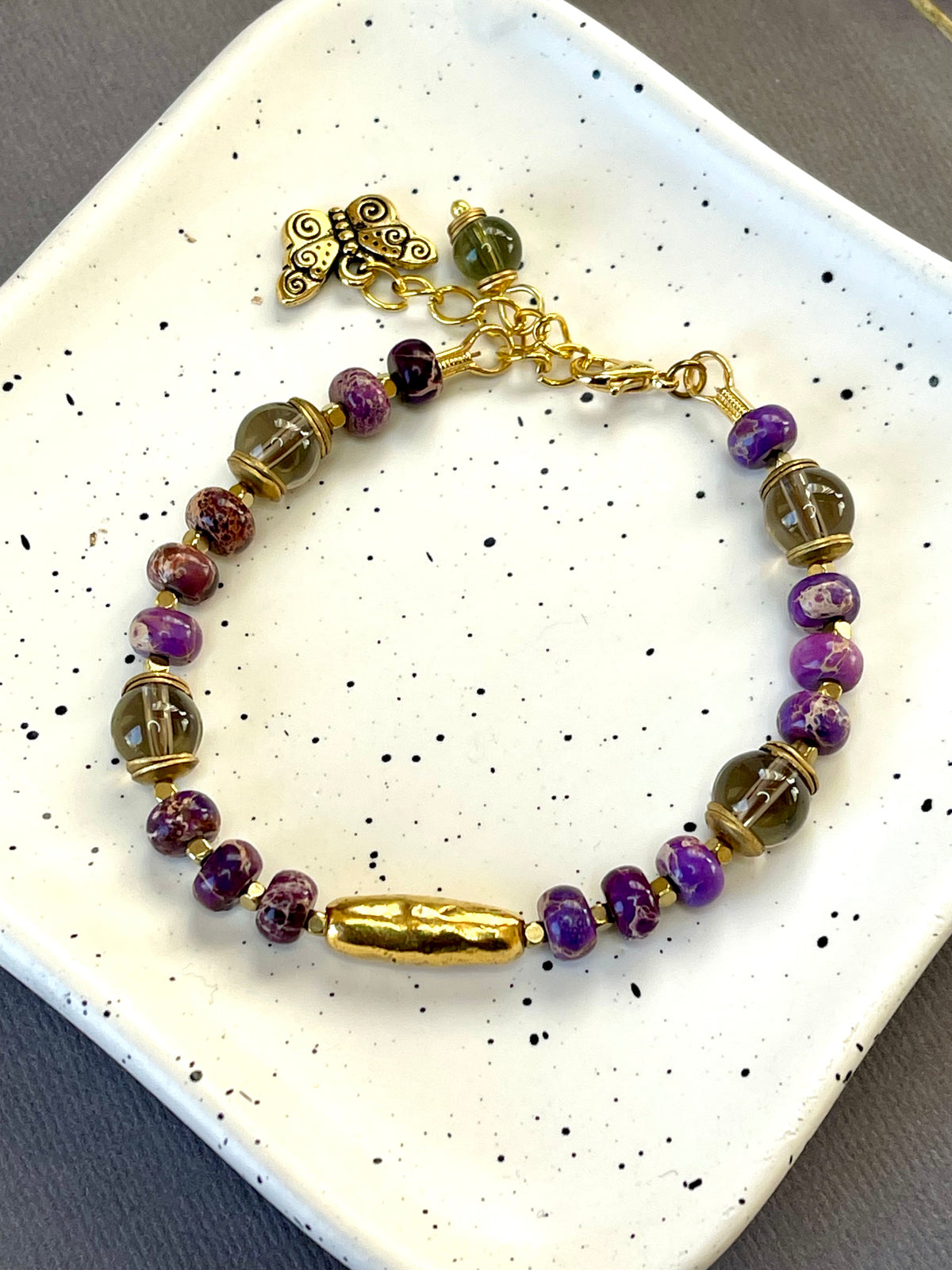 Purple imperial jasper and smoky quartz beaded bracelet with a textured gold tone bar and butterfly charm
