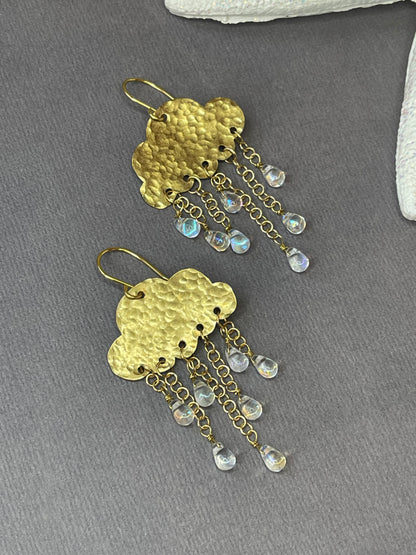 Gold-tone rain cloud dangle earrings with textured brass clouds and dangling raindrop accents on a gray background.