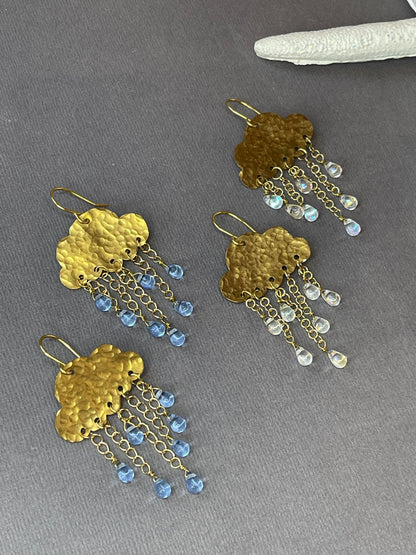 Gold-tone rain cloud dangle earrings with textured brass clouds and dangling raindrop accents on a gray background.