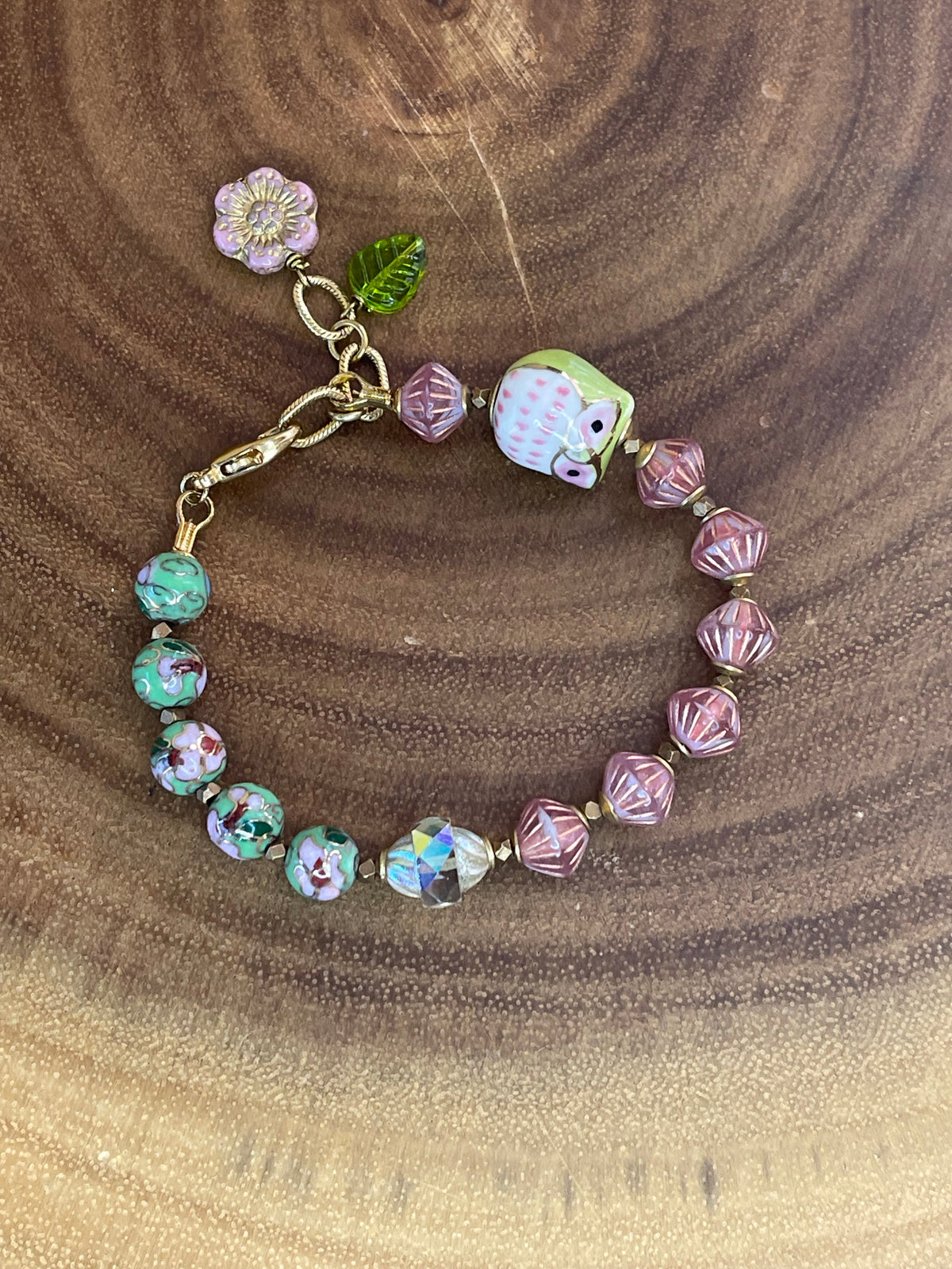 Colorful beaded bracelet with a ceramic owl, pink and green enamel beads, Czech glass beads, flower charm, and green leaf charm.