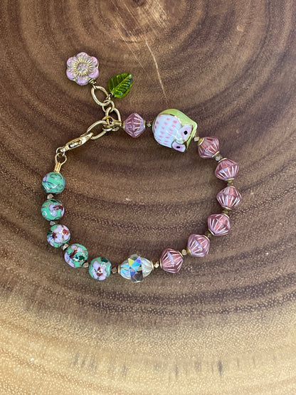 Colorful beaded bracelet with a ceramic owl, pink and green enamel beads, Czech glass beads, flower charm, and green leaf charm.