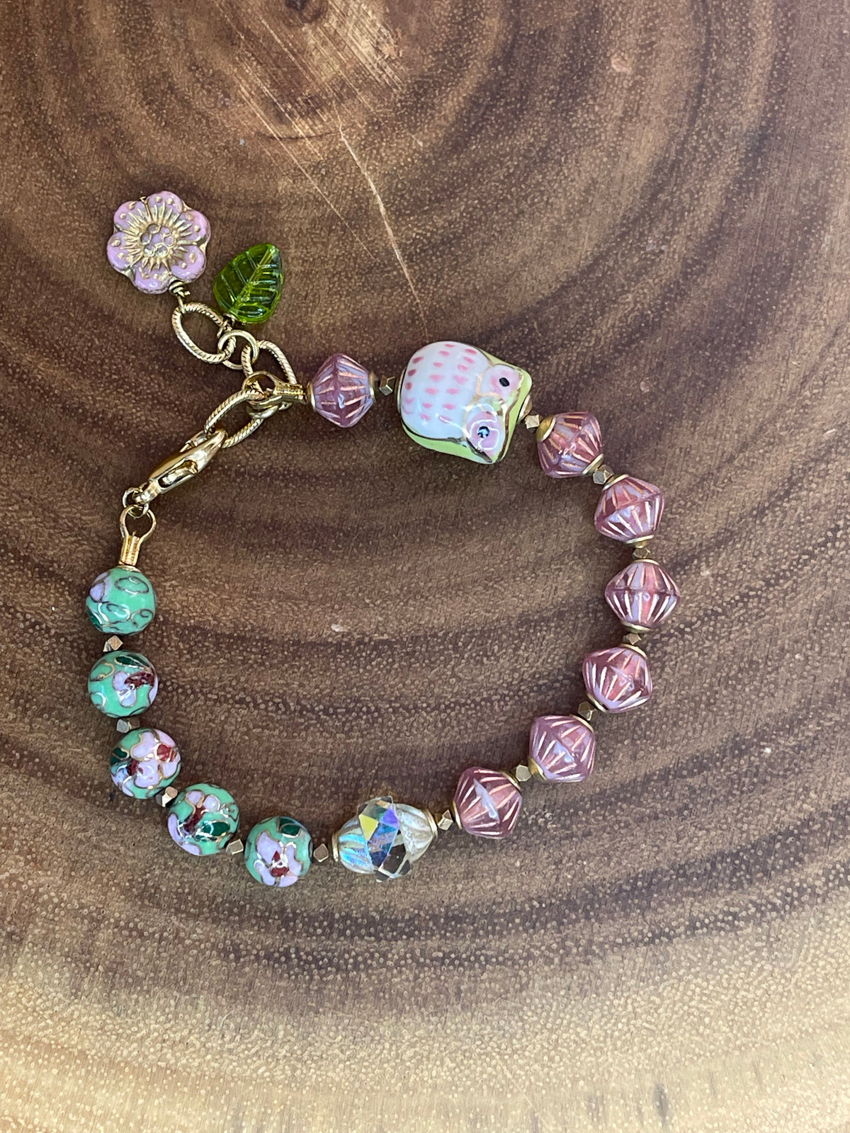 Colorful beaded bracelet with a ceramic owl, pink and green enamel beads, Czech glass beads, flower charm, and green leaf charm.