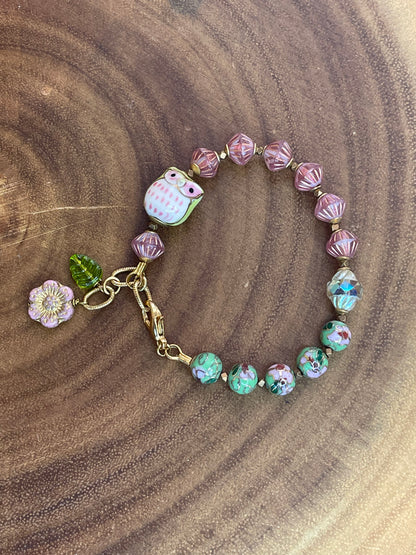 Colorful beaded bracelet with a ceramic owl, pink and green enamel beads, Czech glass beads, flower charm, and green leaf charm.