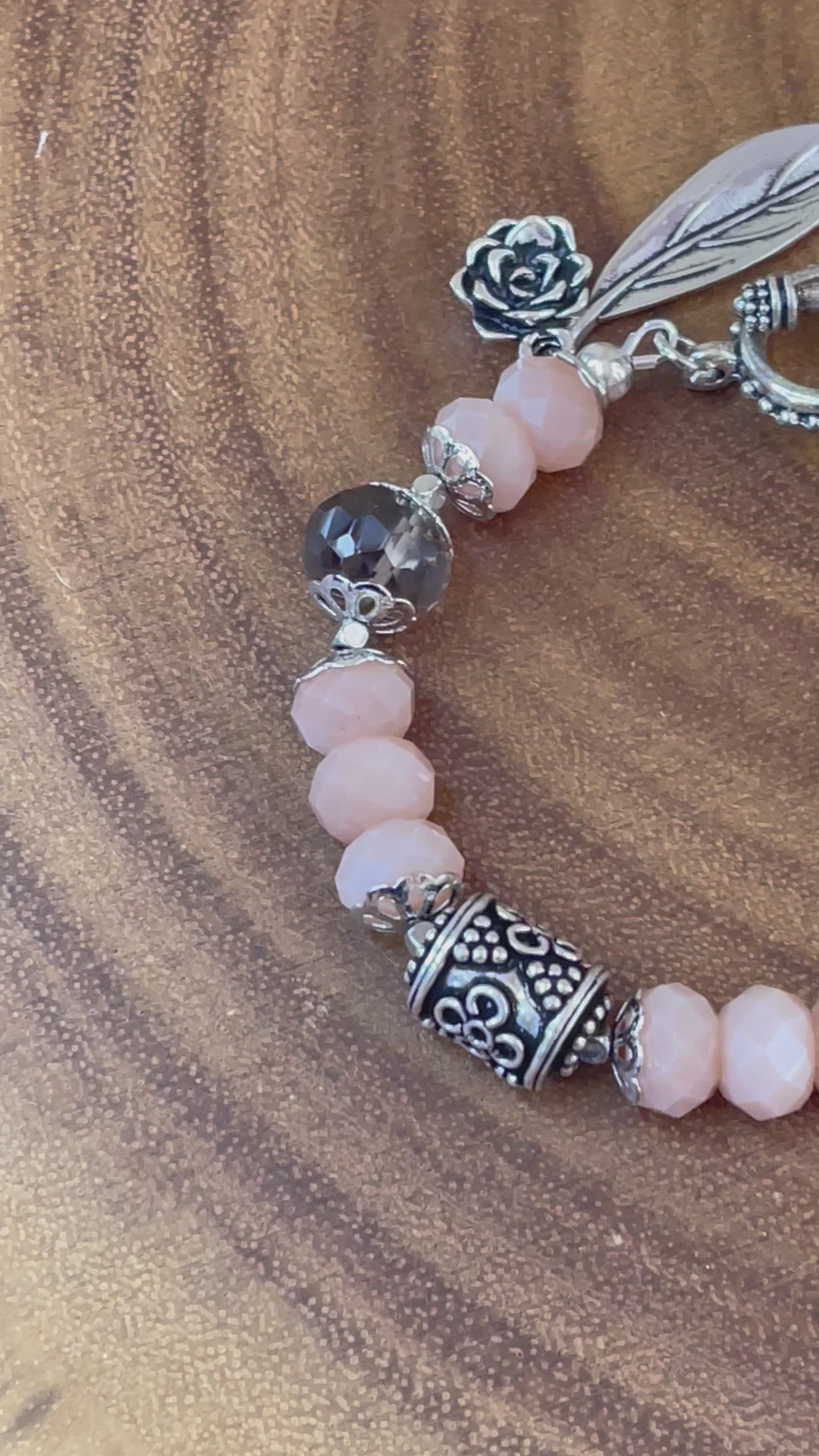 Peach moonstone and smoky quartz beaded bracelet with an ornate silver-plated focal bead, flower and leaf charms, displayed on a wooden surface.