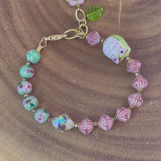 Colorful beaded bracelet with a ceramic owl, pink and green enamel beads, Czech glass beads, flower charm, and green leaf charm.