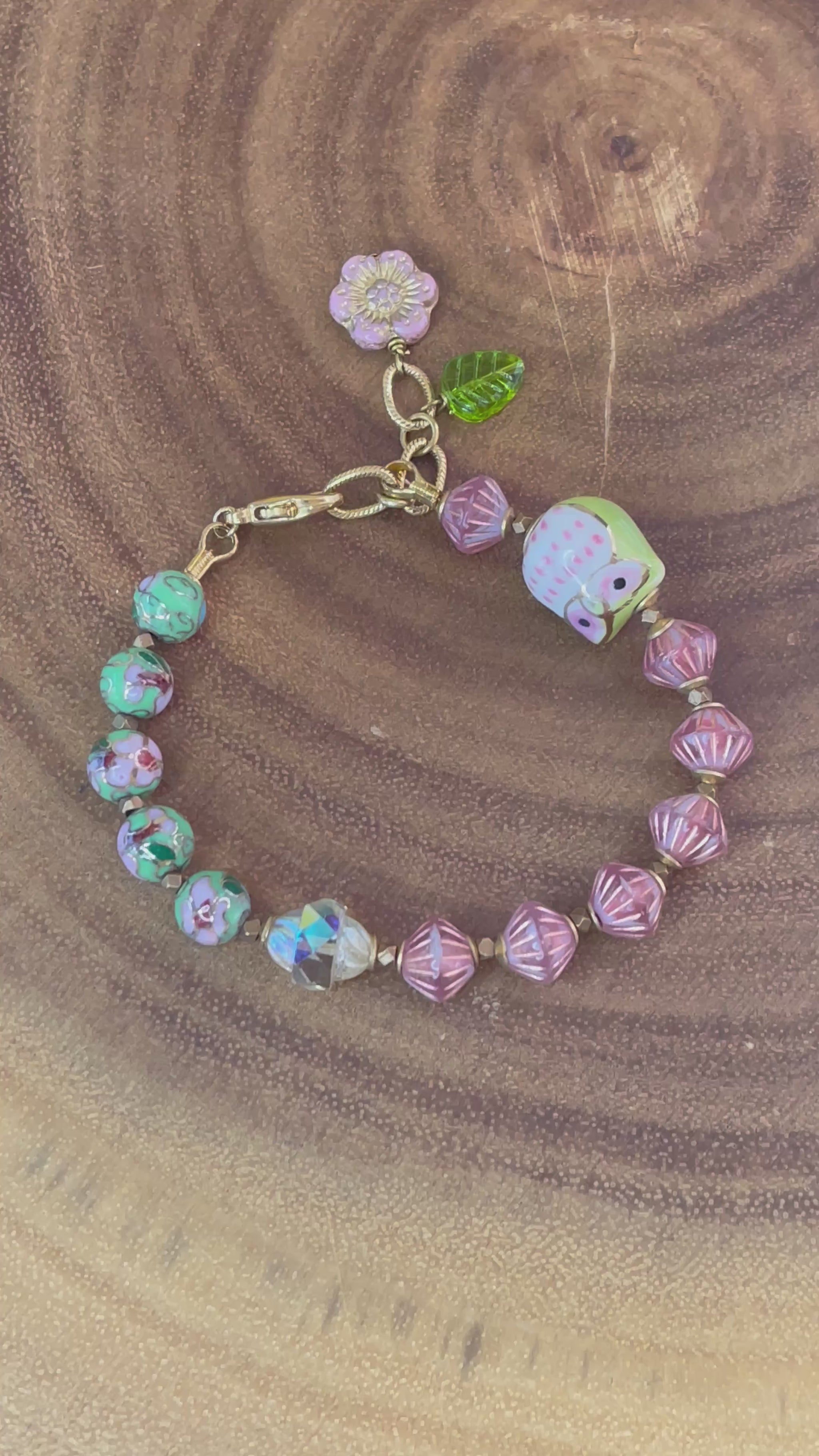 Colorful beaded bracelet with a ceramic owl, pink and green enamel beads, Czech glass beads, flower charm, and green leaf charm.